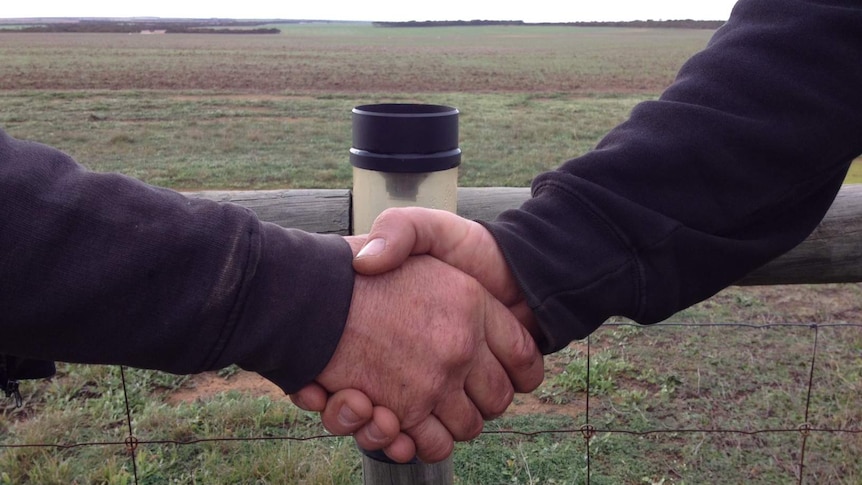 Two men shake hands in front of rain gauge on farming property