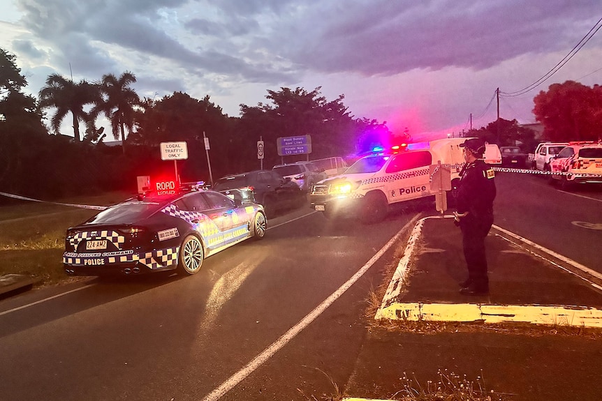 Police cars with lights on block off a street in Cairns at dusk.