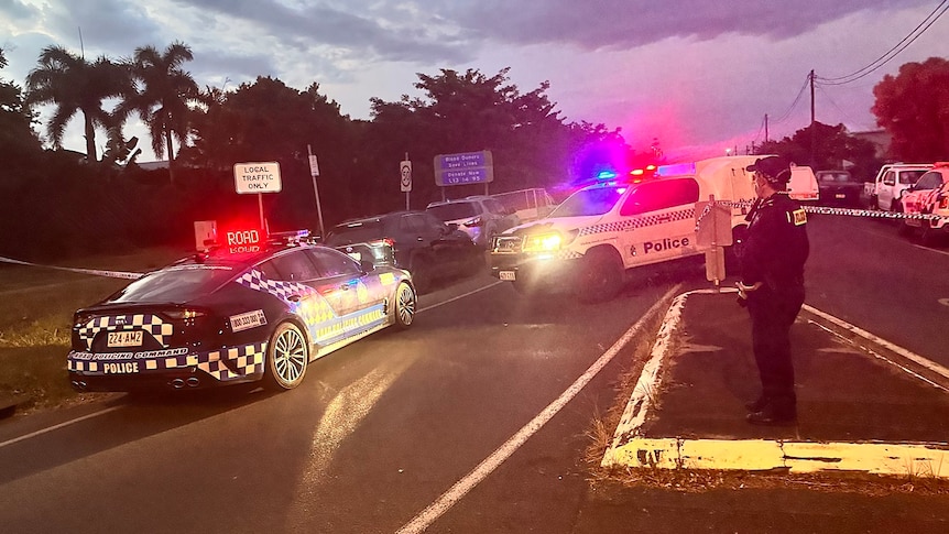 Police cars with lights on block off a street in Cairns at dusk.