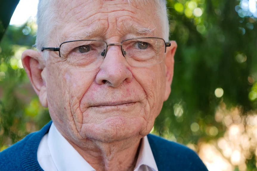 Portrait of man in his 80s in a garden looking off camera with a serious expression.