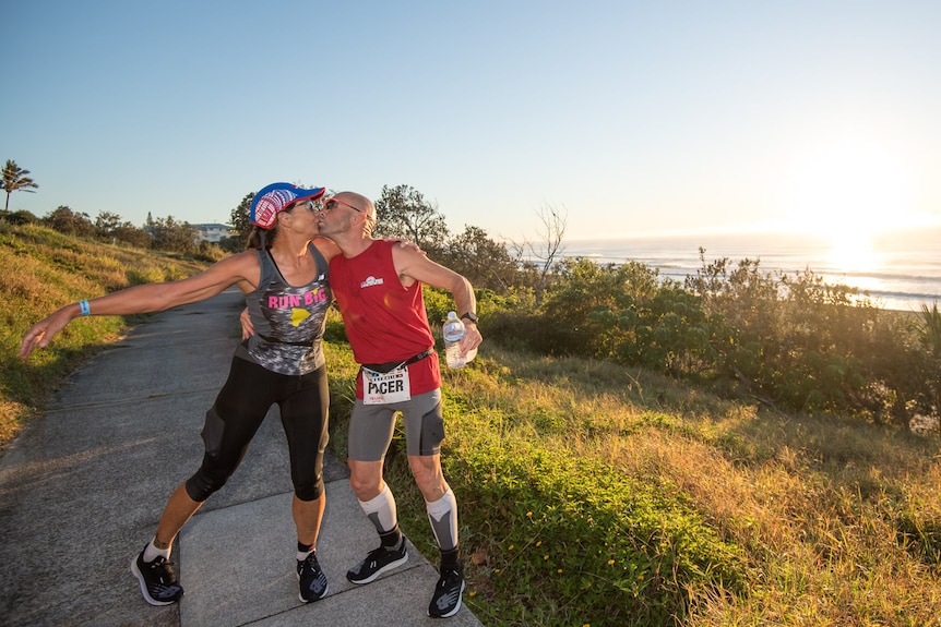 A woman and a man kiss infront of a beach while running in a race 
