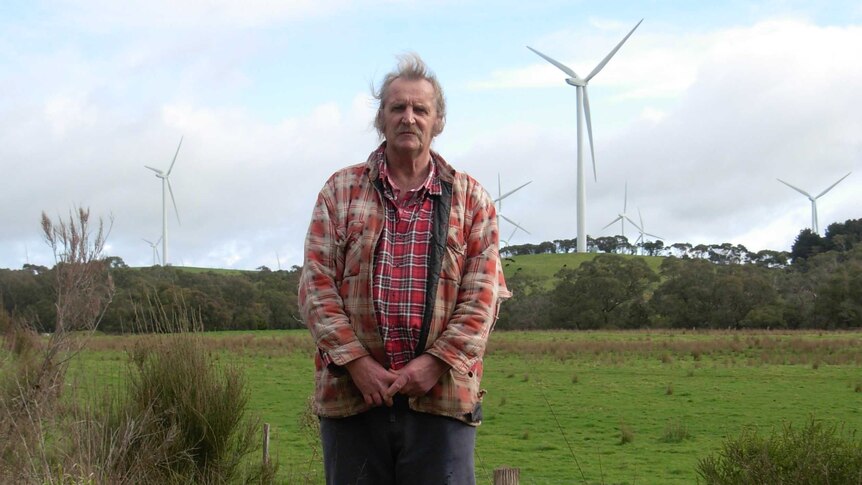 Man John Zakula stands on his property with wind turbines in the background