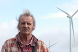 Man stands on his property with wind turbines in the background