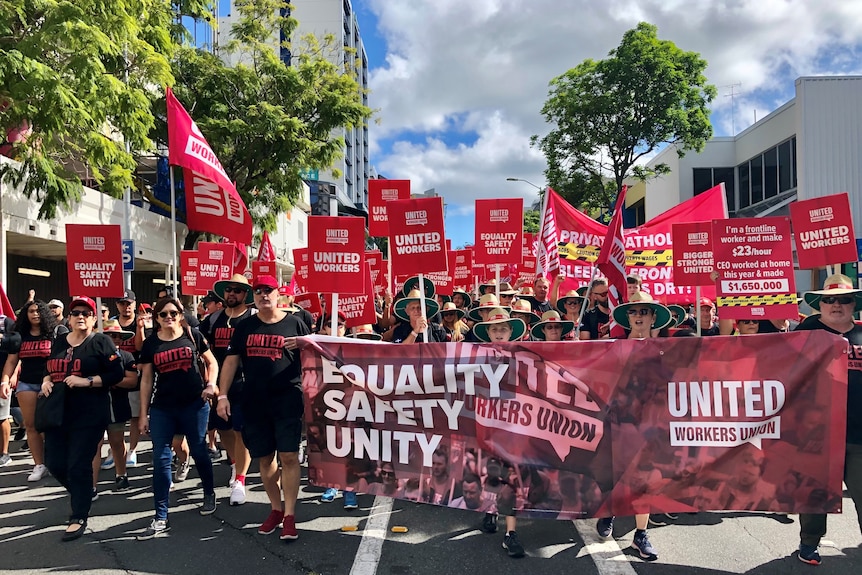 Large crowds carrying red and maroon signs reading Equality Safety Unity. 