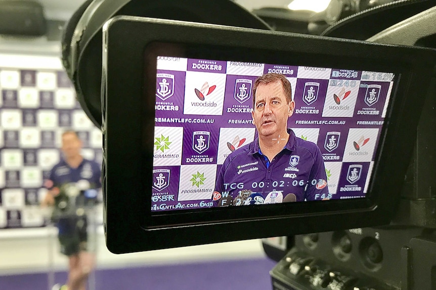 Fremantle coach Ross Lyon on a TV camera screen at a press conference
