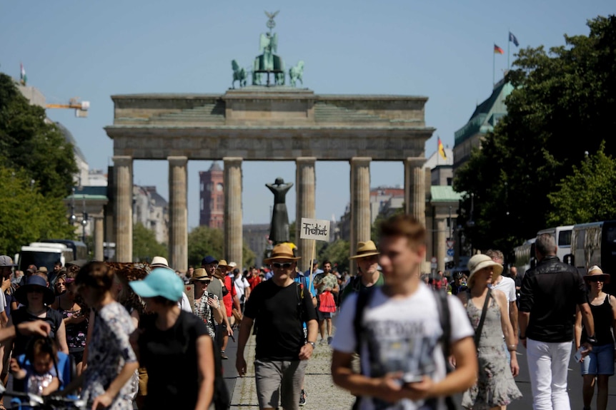 Protesters move along a sunny road with a large city gate seen in the background.