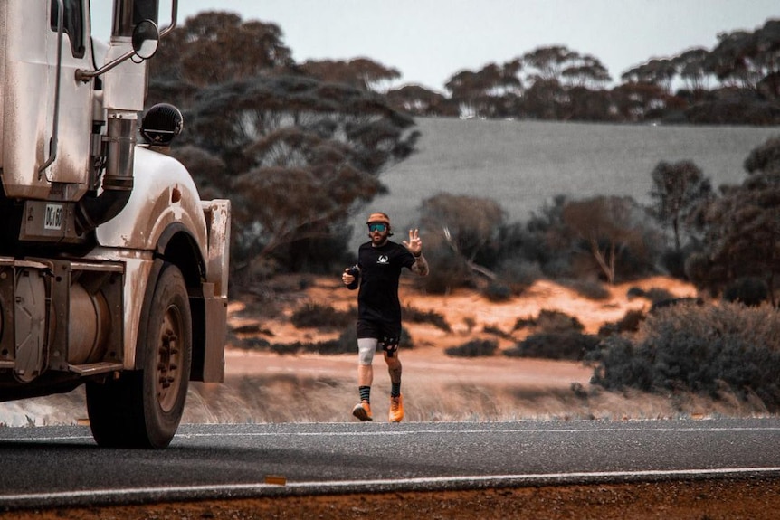Man waves while running on the side of the road as truck passes.