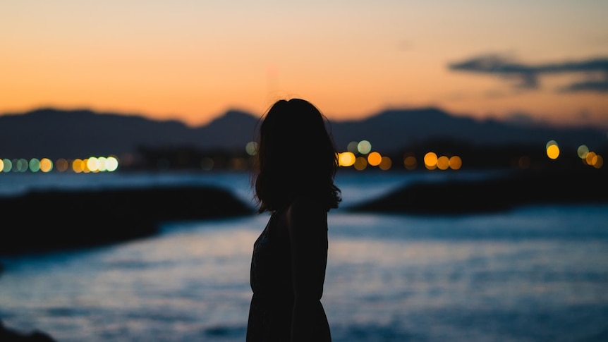 Silhouette of woman at dusk in front of a body of water