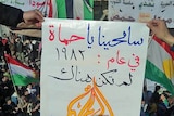 Protesters march in the Syrian town of Amoda as people hold a sign saying "Forgive us Hama".