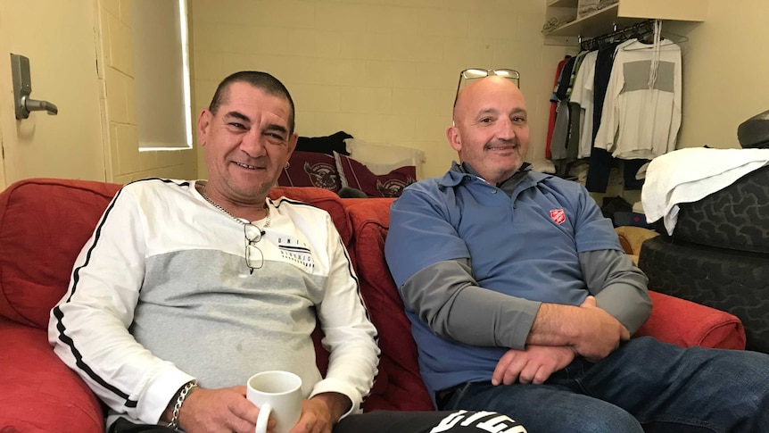 Two men sit on a couch in a shared house