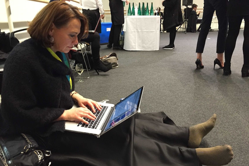 Millar sitting on floor with shoes off writing story on laptop.