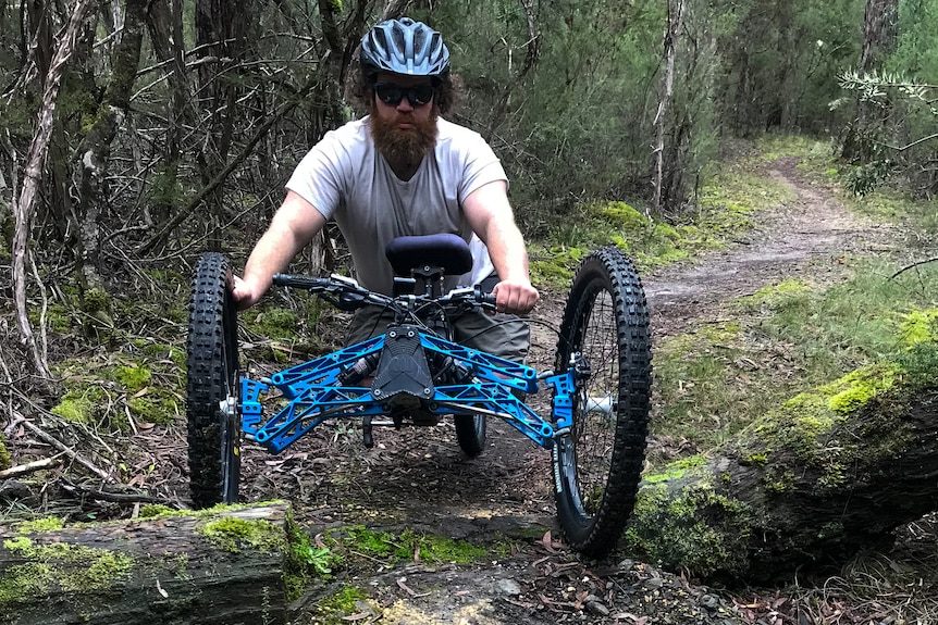 a man crosses a log in an adaptive bike. 