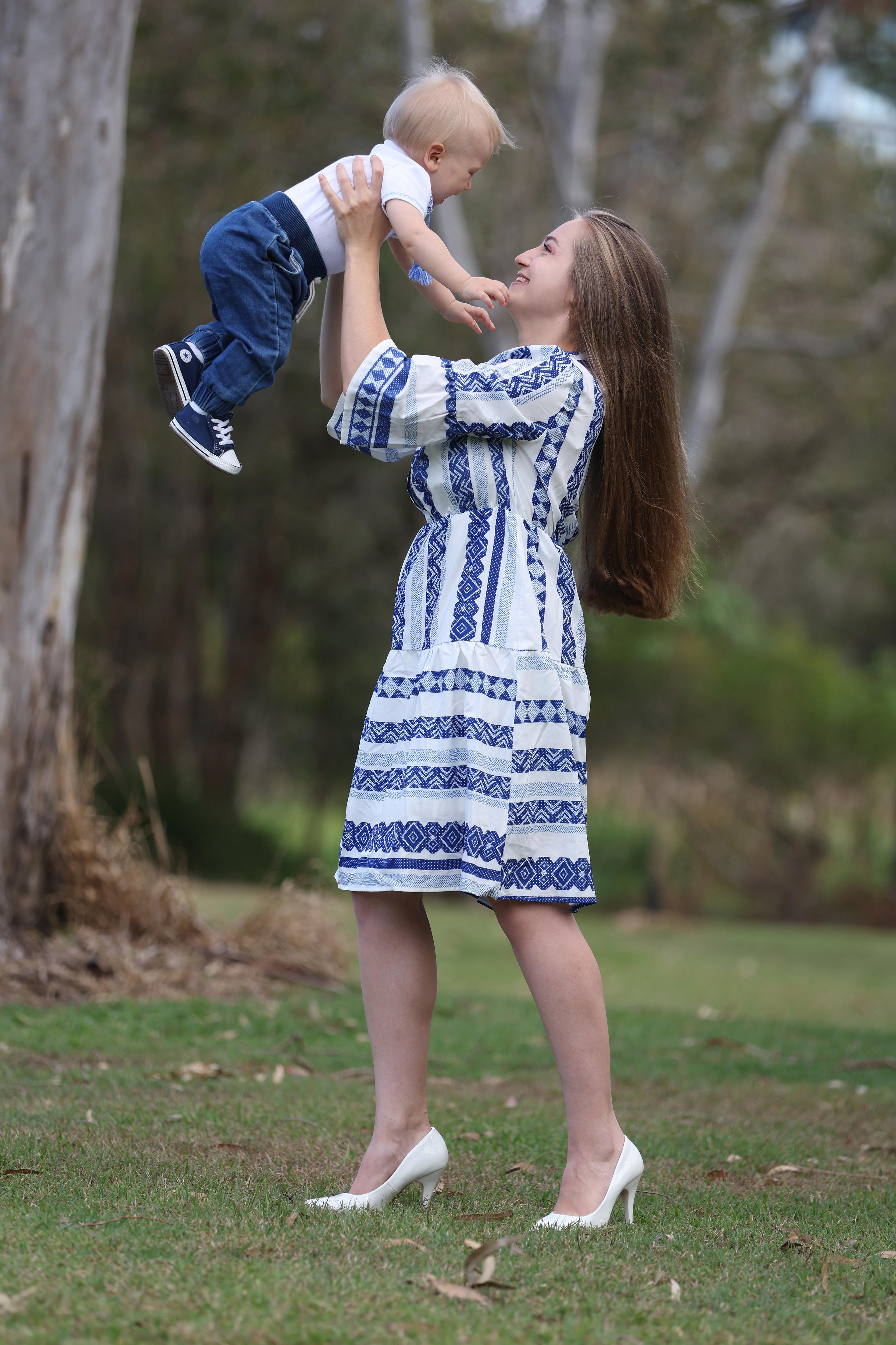 a mother holds her baby son high in the air, they are both smiling and laughing