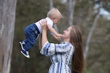 a mother holds her baby son high in the air, they are both smiling and laughing