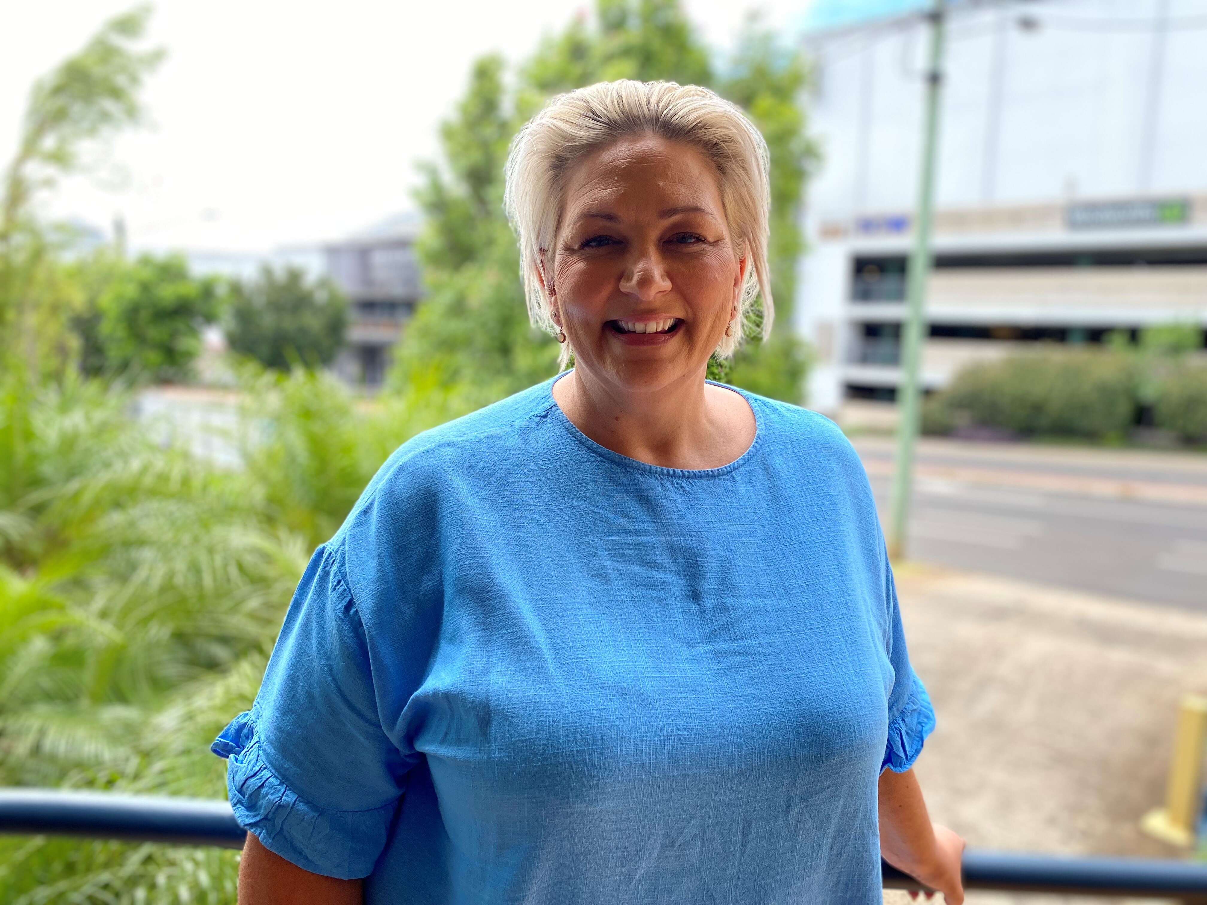 A blonde woman in a blue shirt smiles at the camera