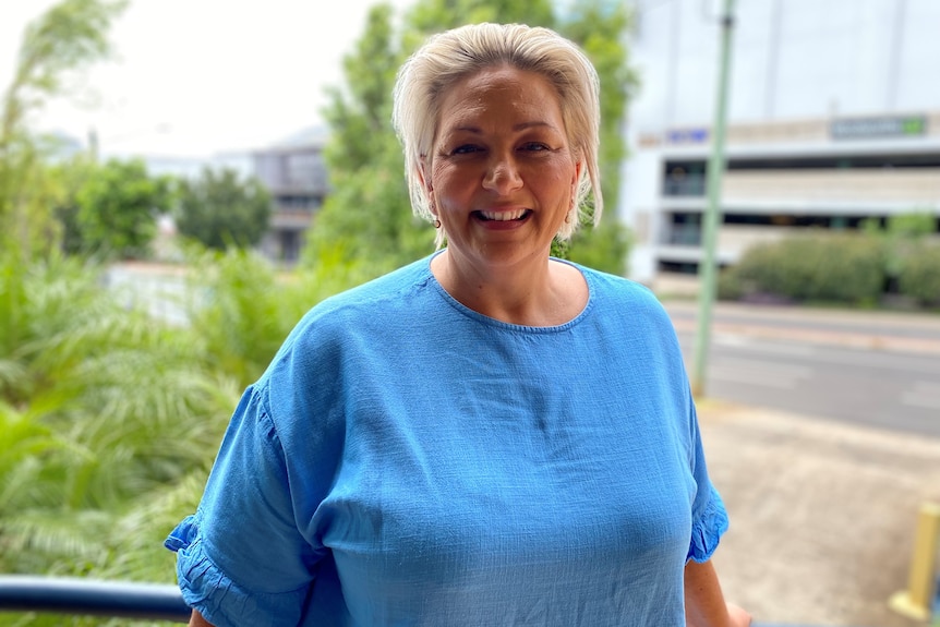 A blonde woman in a blue shirt smiles at the camera