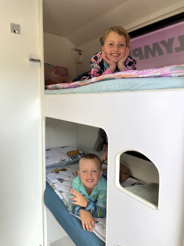 a young girl and boy lay in bunk beds smiling in a caravan