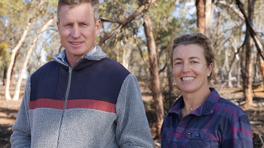 A man and woman in work shirts smile broadly in a bush setting  