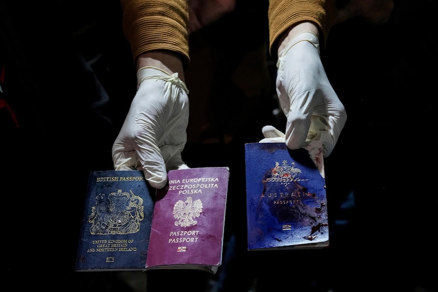 A photo of a pair of gloved hands holding up three bloodied passports. One British, one Polish and one Australian.