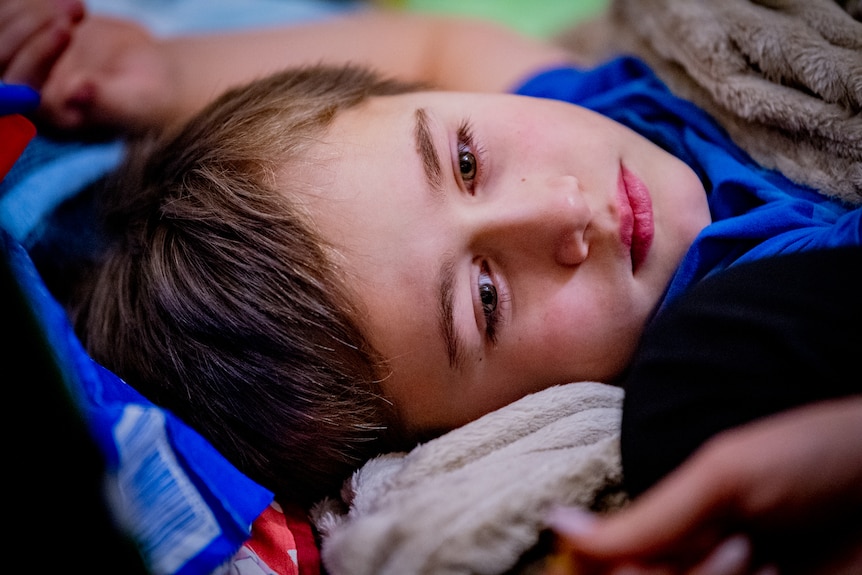 Dima is laying down in his bed. Close up of his face, soft expression, brown eyes.  