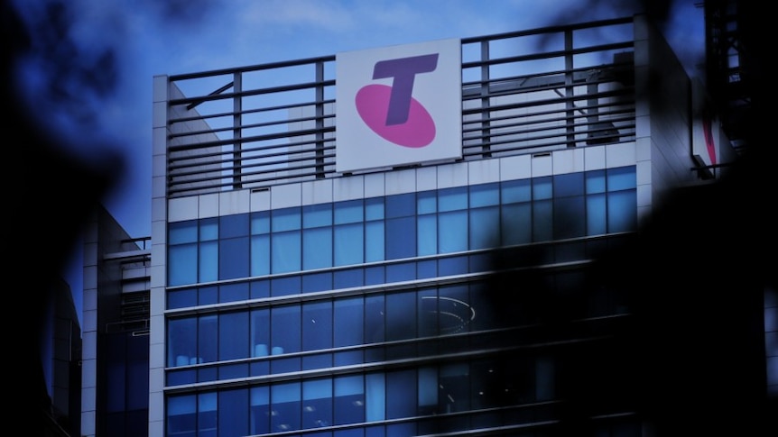 A Telstra logo on the side of a building through some trees.