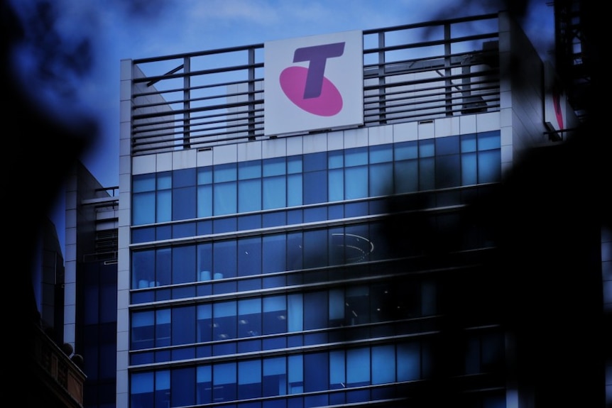 A Telstra logo on the side of a building through some trees.