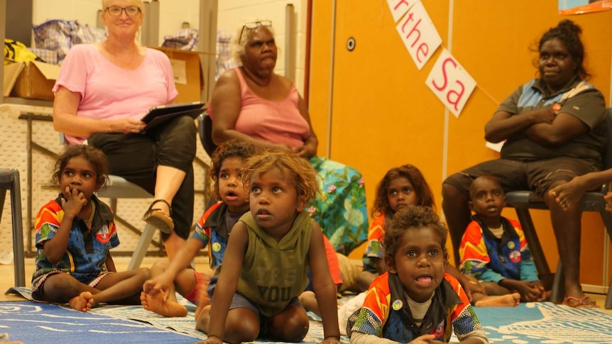 Small Aboriginal children in classroom on mat with adults sitting in chairs