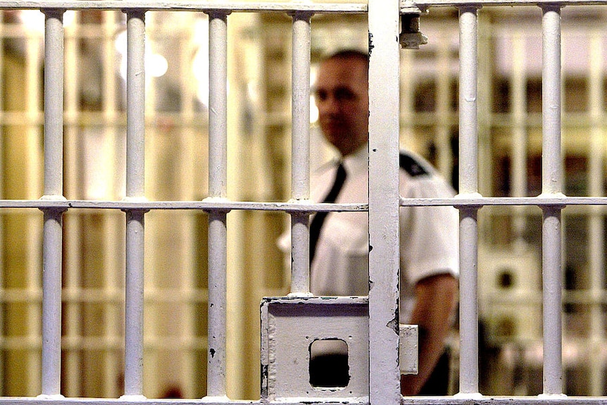 A prison guard is seen through the bars of a prison cell.
