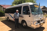Older man standing next to a white school bus 