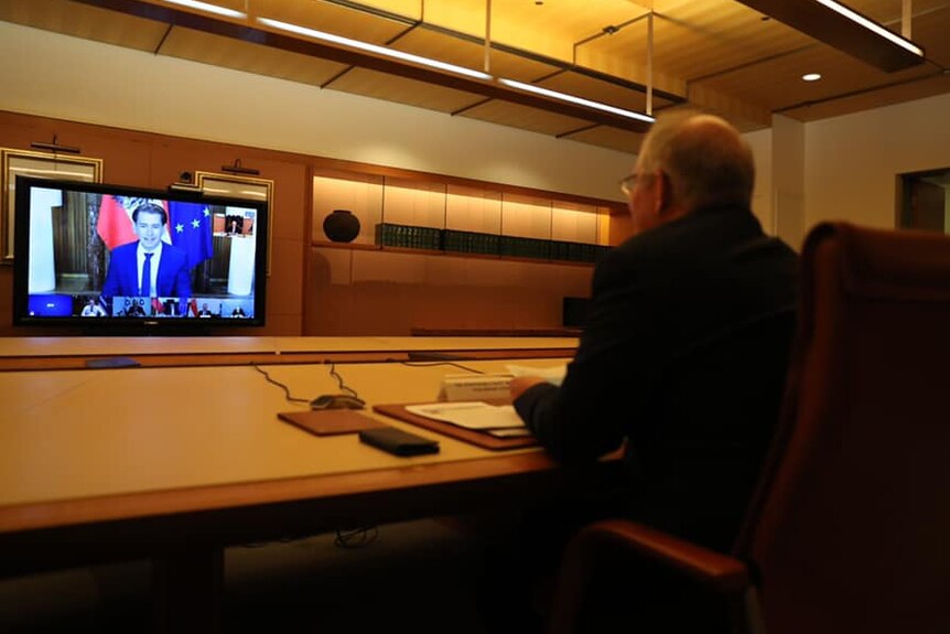 Scott Morrison sits at a large desk looking towards a monitor