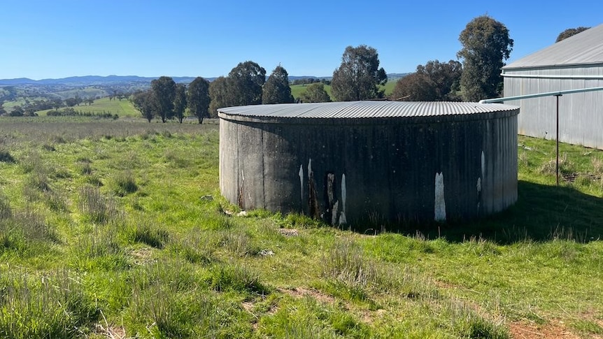 A concrete water tank lies unused in a paddock