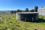 A concrete water tank lies unused in a paddock
