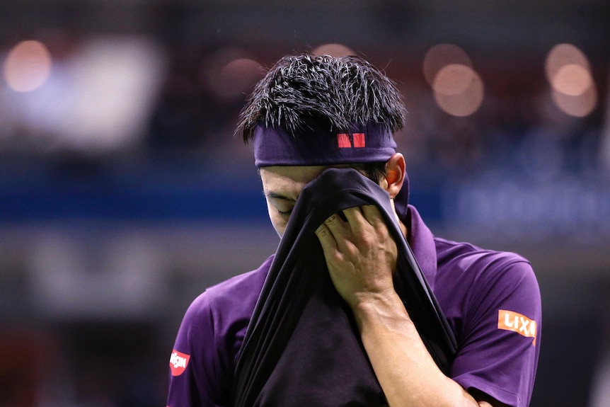 A male tennis player wipes his face with his navy blue shirt