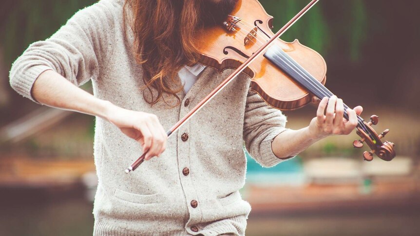A person playing a violin in a cream cardigan.