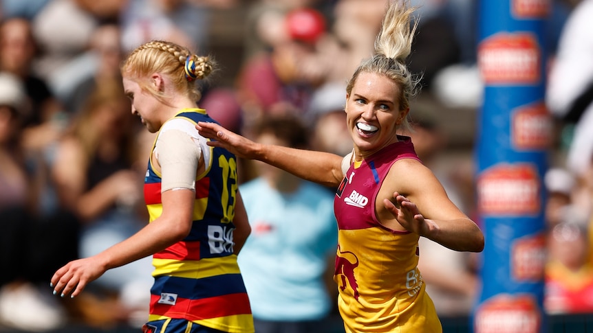 A grinning Brisbane AFLW player runs back down the ground after kicking a goal in finals.