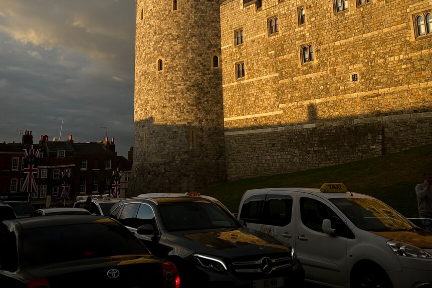 Sun is shining onto the wall of the castle, as traffic passes by in the shadows. 