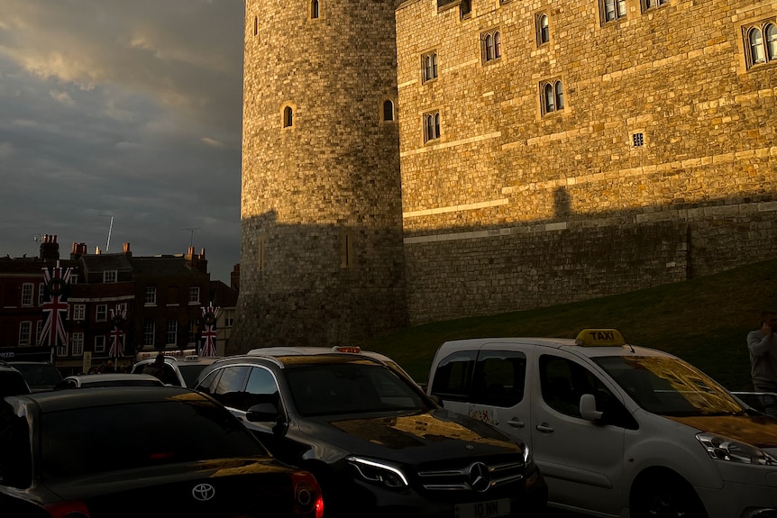 Sun is shining onto the wall of the castle, as traffic passes by in the shadows. 