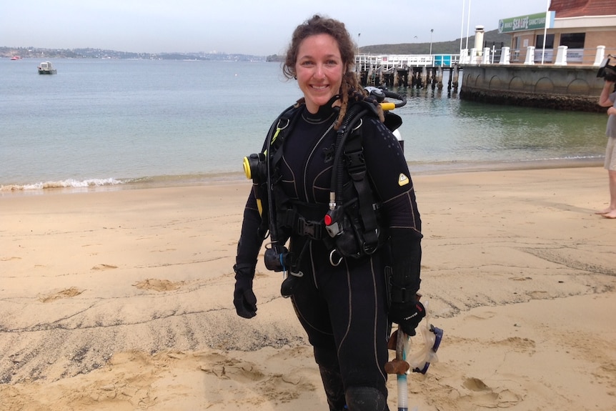 A woman wearing diving gear stands on a Sydney beach.