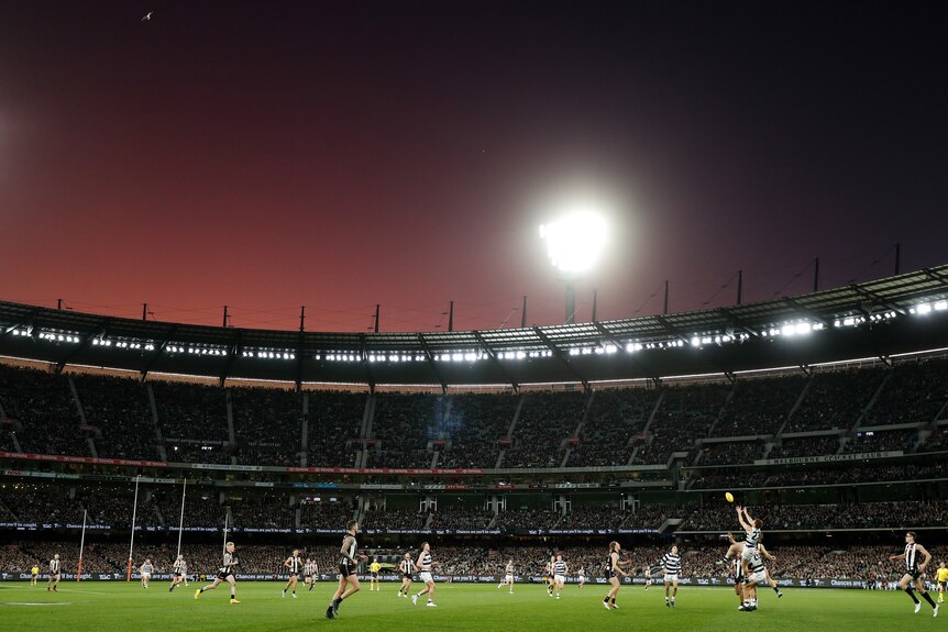 The sun sets over the MCG while a football game is being played