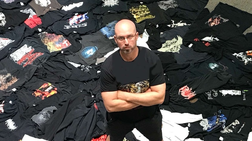 Photo of a bald man wearing a black metal t-shirt surround by other t-shirts