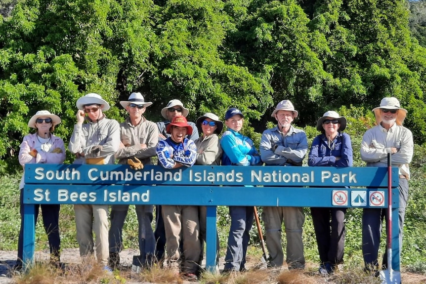 a group of people wearing hats and long sleeved shirts stand behind a sign saying "St Bees Island"