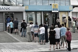 People stand in a queue to use ATM machines to withdraw cash at a bank in Athens