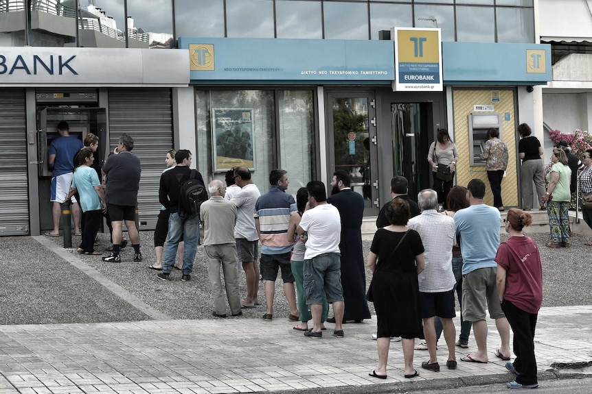 People stand in a queue to use ATM machines to withdraw cash at a bank in Athens