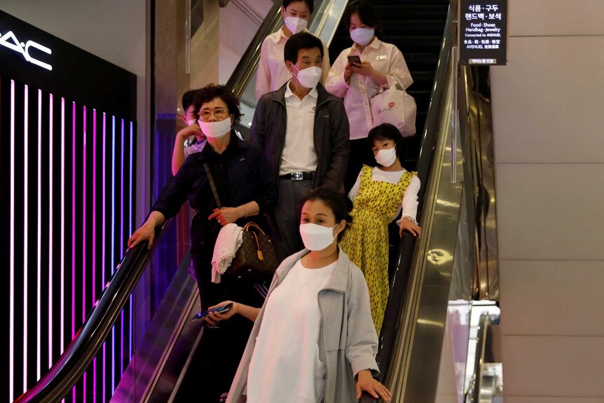 Shoppers at a South Korean store ride an escalator while wearing masks