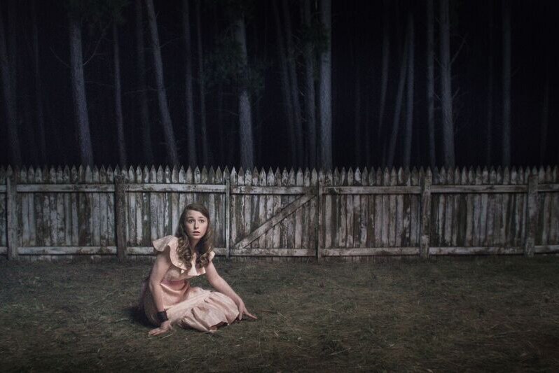 Image of actor Bethany Whitmore on the ground in a backyard next to a forest in scene from the Australian film Girl Asleep.