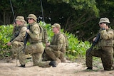 Four army troops with radios and guns on beach