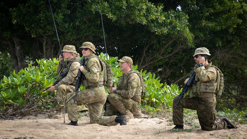 Four army troops with radios and guns on beach