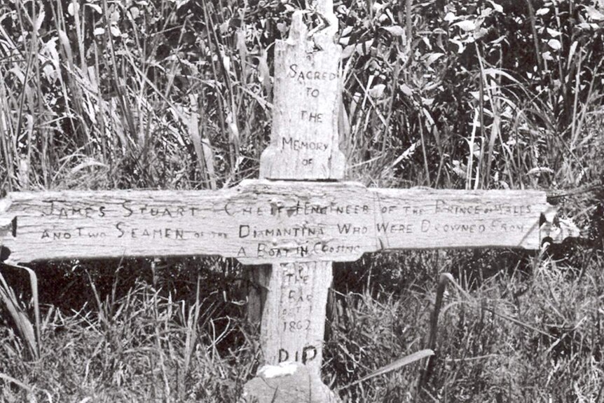 A wooden cross over a grave site, with hand engraved writing.