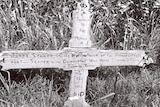 A wooden cross over a grave site, with an inscription engraved on it.