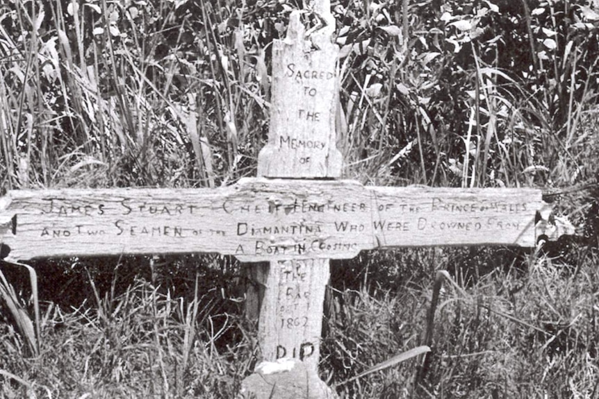 A wooden cross over a grave site, with an inscription engraved on it.